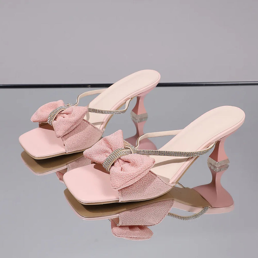 Blush pink heeled mules with crystal bow detail and square toe.