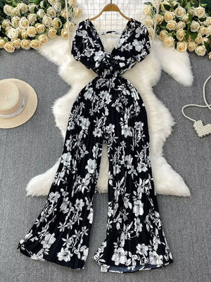 Black floral print cotton romper with V-neck, short sleeves, and wide pleated legs.