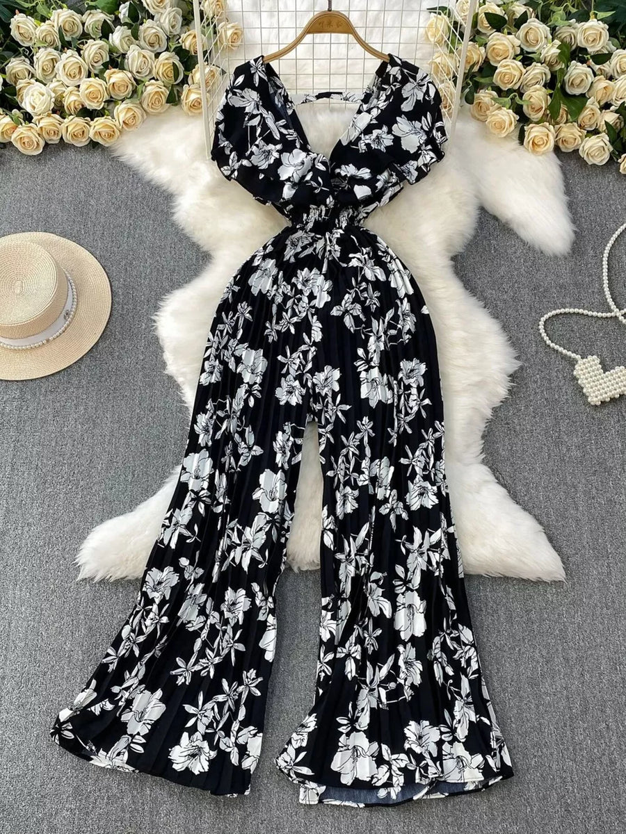 Black floral print cotton romper with V-neck, short sleeves, and wide pleated legs.