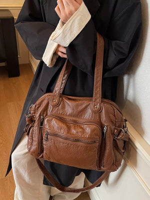 Brown faux leather satchel bag with multiple zippered pockets and top handles.