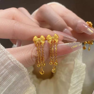 Gold bowknot tassel earrings with heart charms and delicate chains.