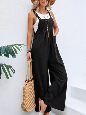 Black wide-leg romper with pockets and adjustable straps, styled with a white tank top.