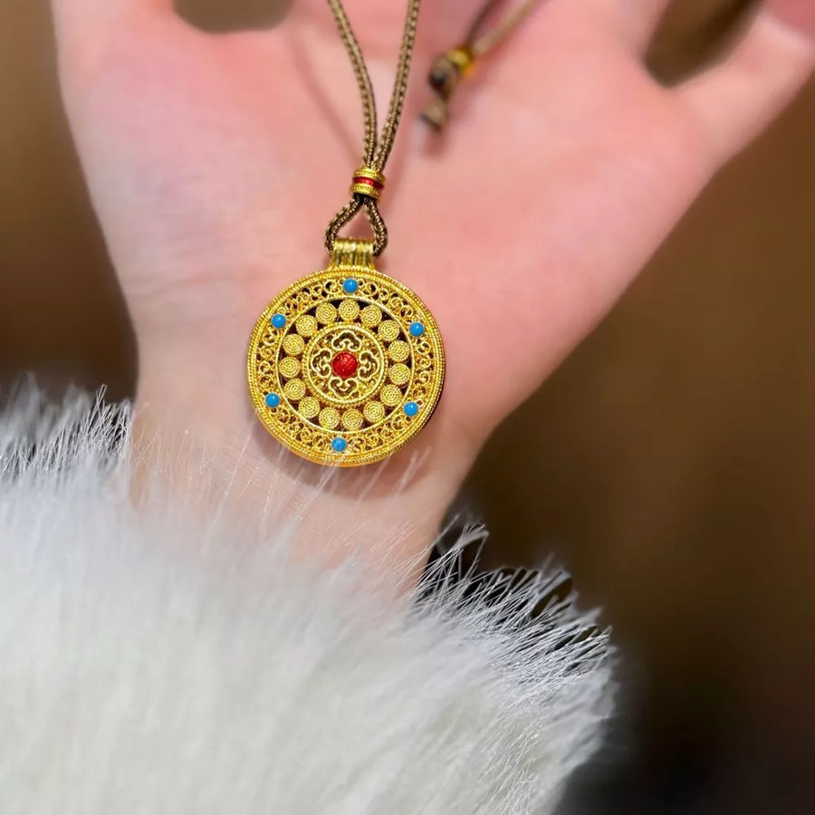 Gold-plated round pendant necklace with red and blue stones on a cord chain.