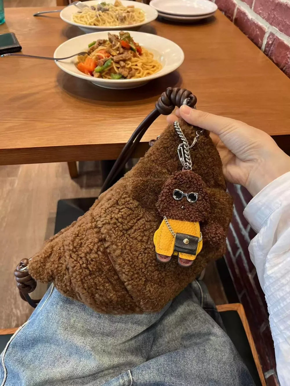Brown plush crossbody bag with knot strap and dog charm accessory.