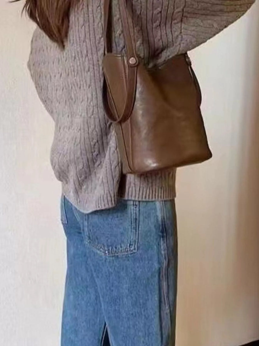 Elegant coffee brown PU leather bucket bag with a single strap, worn with a cable knit sweater and jeans.