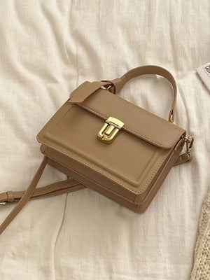 Small coffee pu leather crossbody bag with gold clasp and top handle.