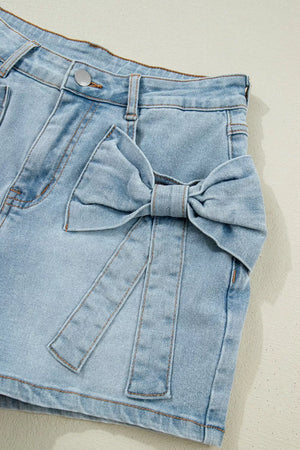 Light wash denim shorts with a large bow detail on the side and button fly.