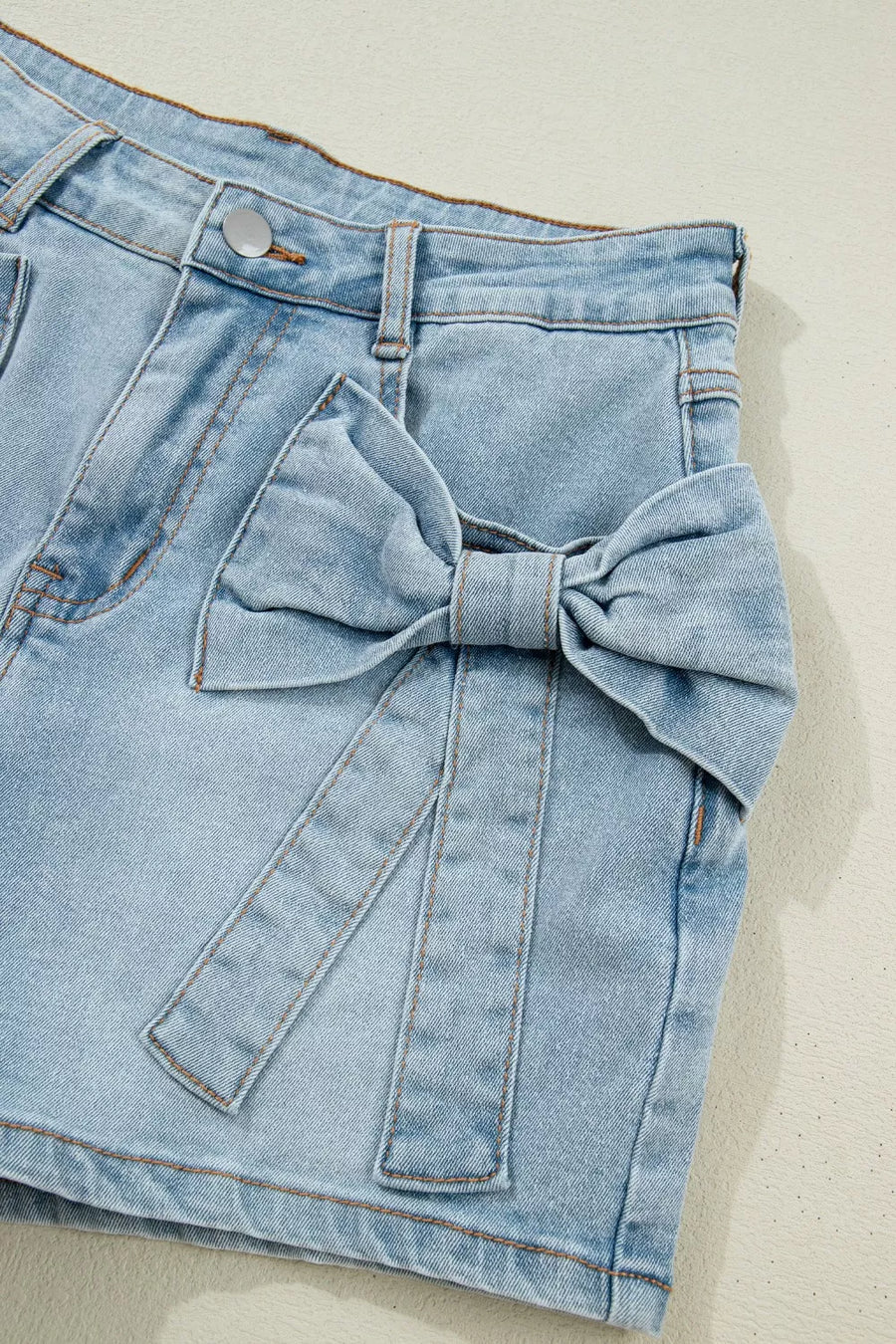 Light wash denim shorts with a large bow detail on the side and button fly.
