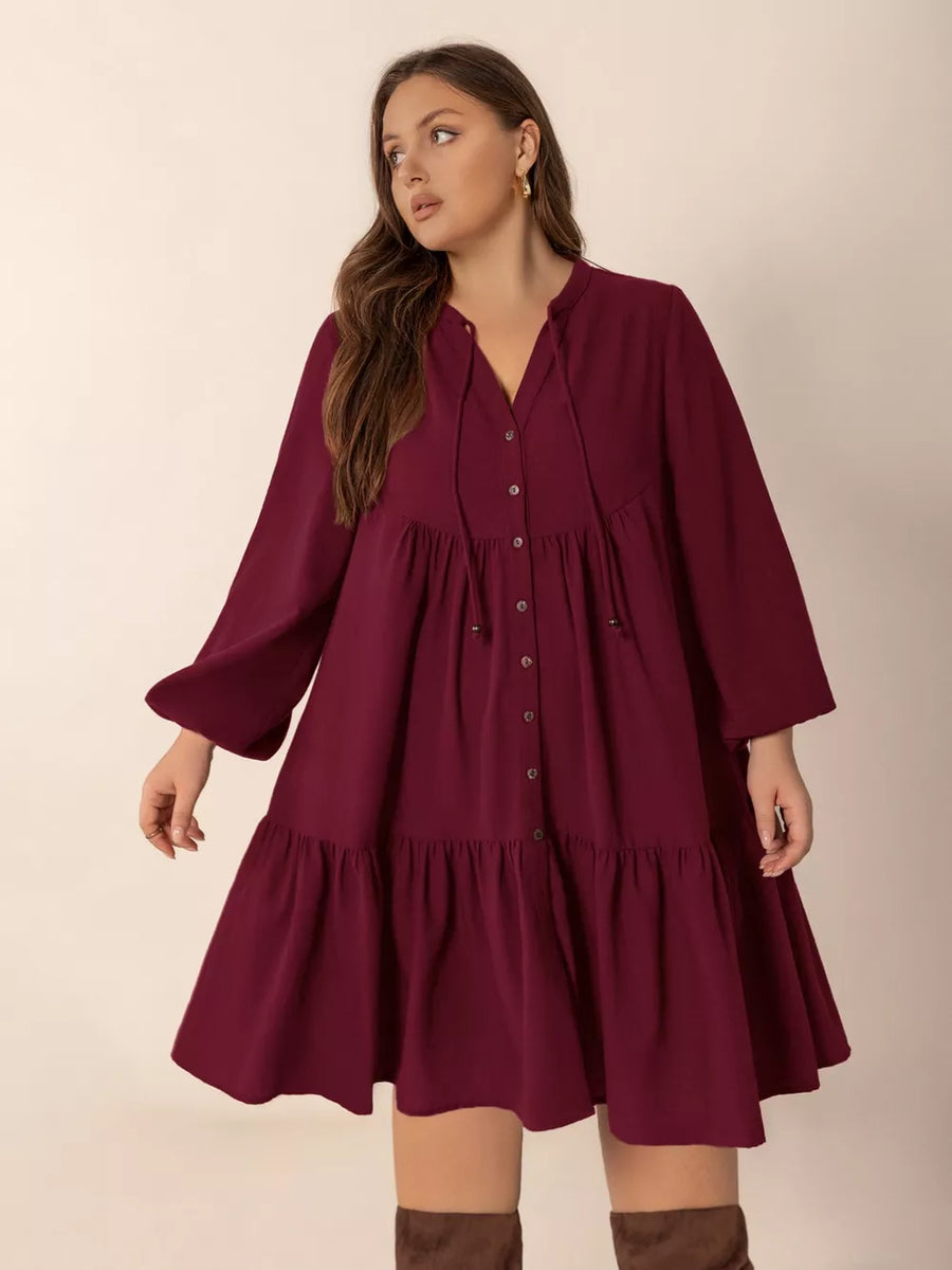 Plus-size burgundy tiered button-front dress with tie-neck and balloon sleeves.