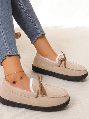 Caramel suede moccasin slippers with white faux fur lining and bow detail.