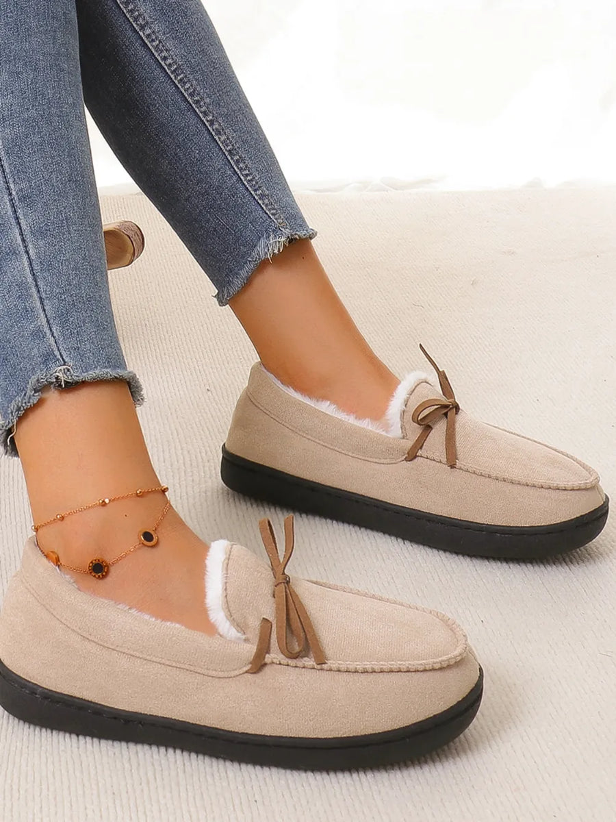 Caramel suede moccasin slippers with white faux fur lining and bow detail.