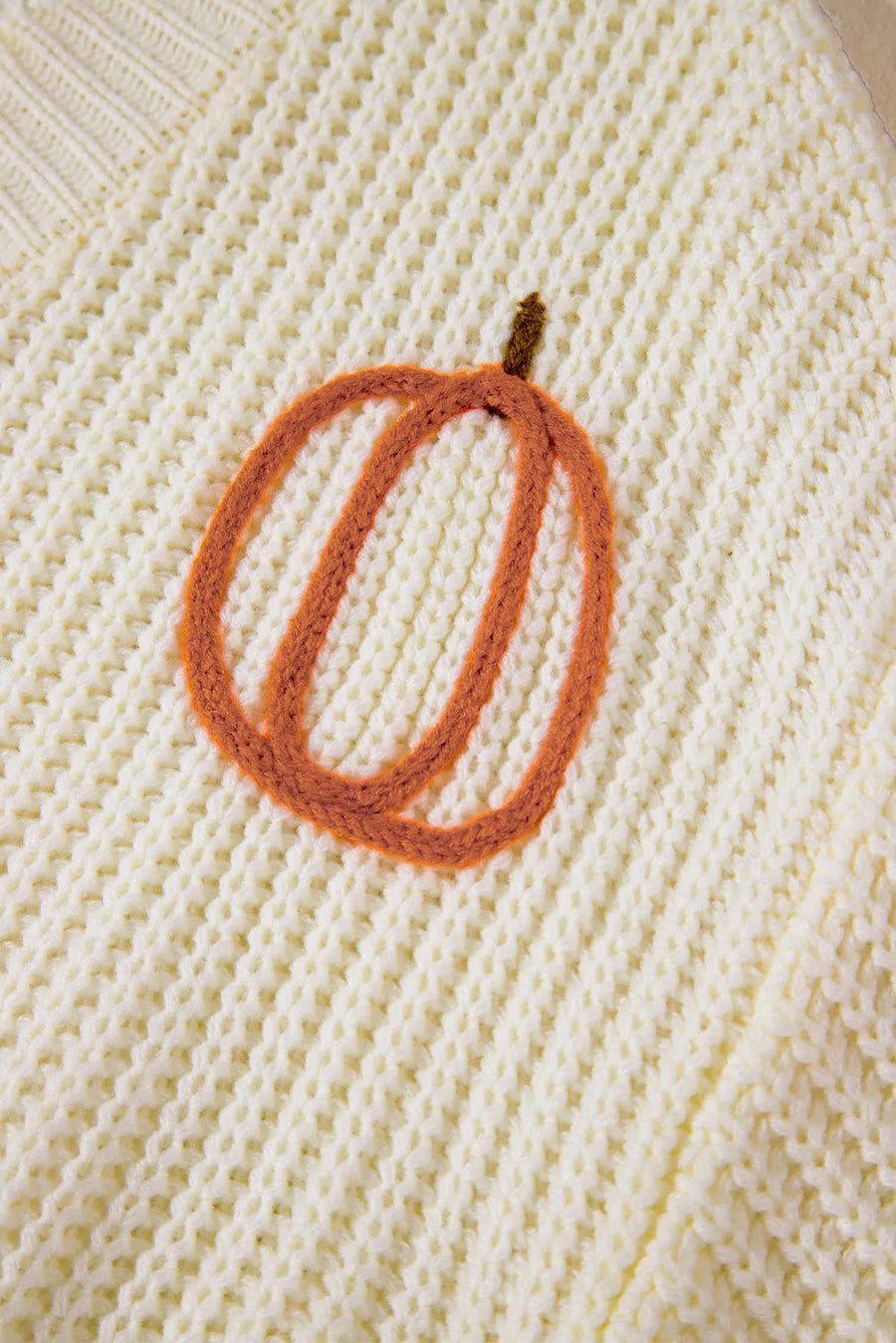 Beige knit sweater with embroidered pumpkin detail.