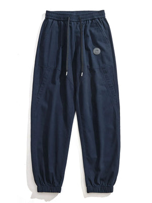 Navy blue relaxed fit joggers with drawstring and elastic cuffs, featuring a circular mountain logo patch.