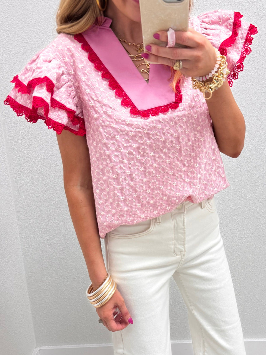 Pink eyelet embroidered blouse with flutter sleeves and red lace trim.