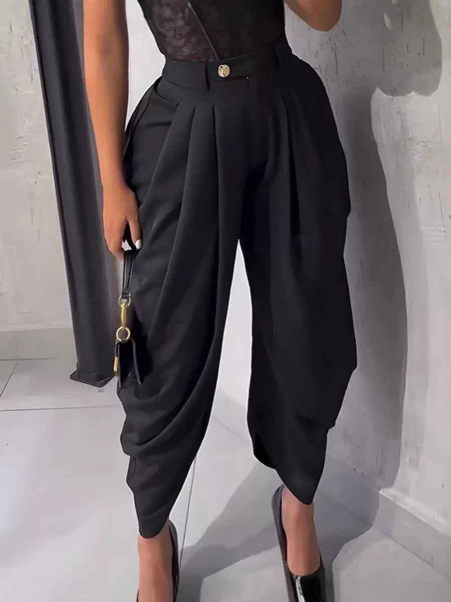 Black high-waisted pants with sculptural pleats and a button detail.