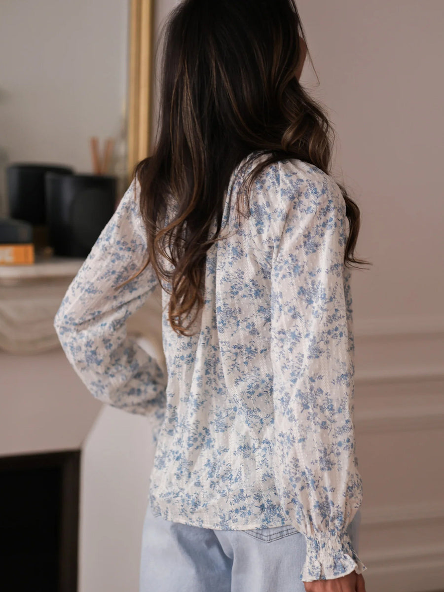 White and blue floral print long-sleeve blouse with tie neck and ruffled cuffs.