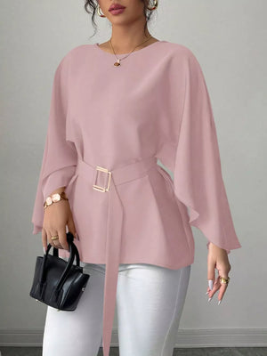 Pink belted blouse with batwing sleeves and gold buckle detail, styled with white pants.