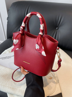 Red pu leather bucket bag with heart print scarf tied on handles and detachable strap.