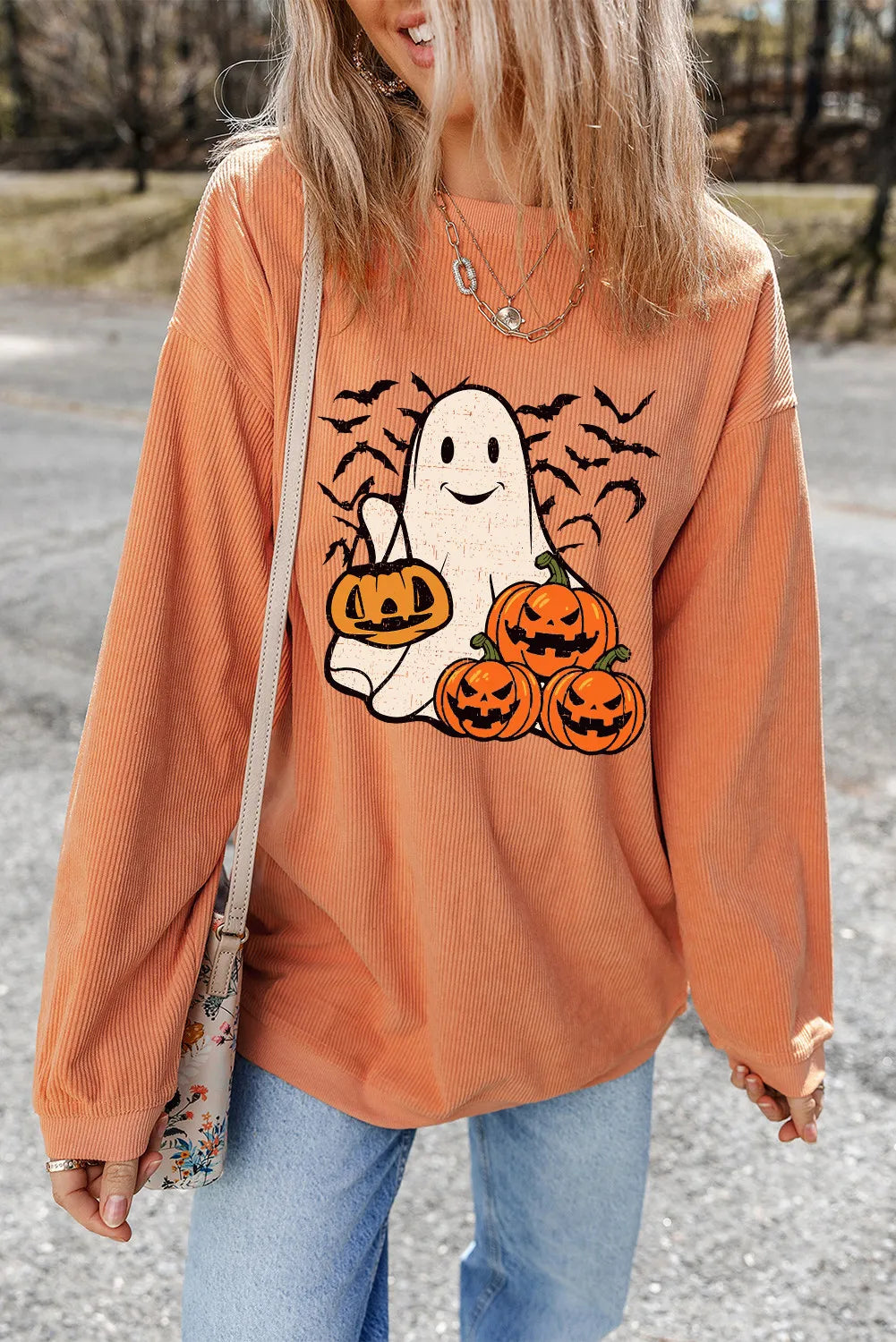 Corduroy crewneck sweatshirt in sherbet orange with a ghost and pumpkin graphic and bats.