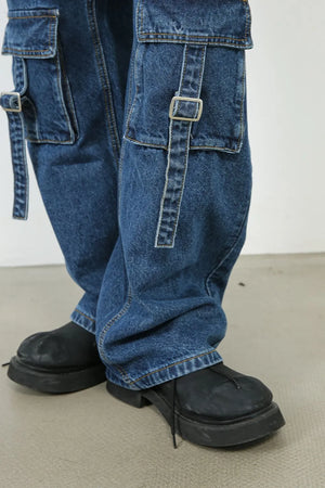 Medium wash denim cargo pants with buckle strap pockets and wide legs.