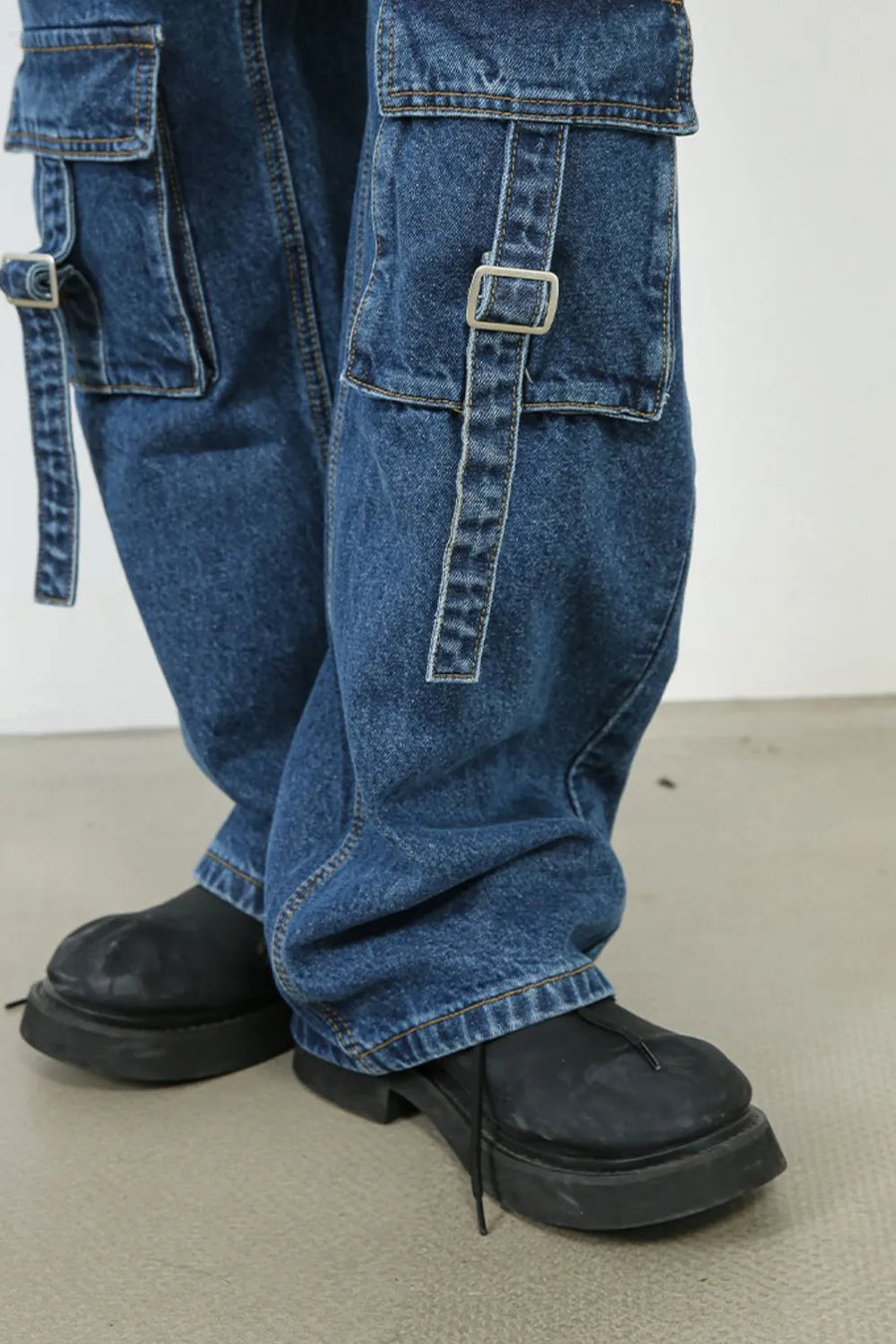 Medium wash denim cargo pants with buckle strap pockets and wide legs.
