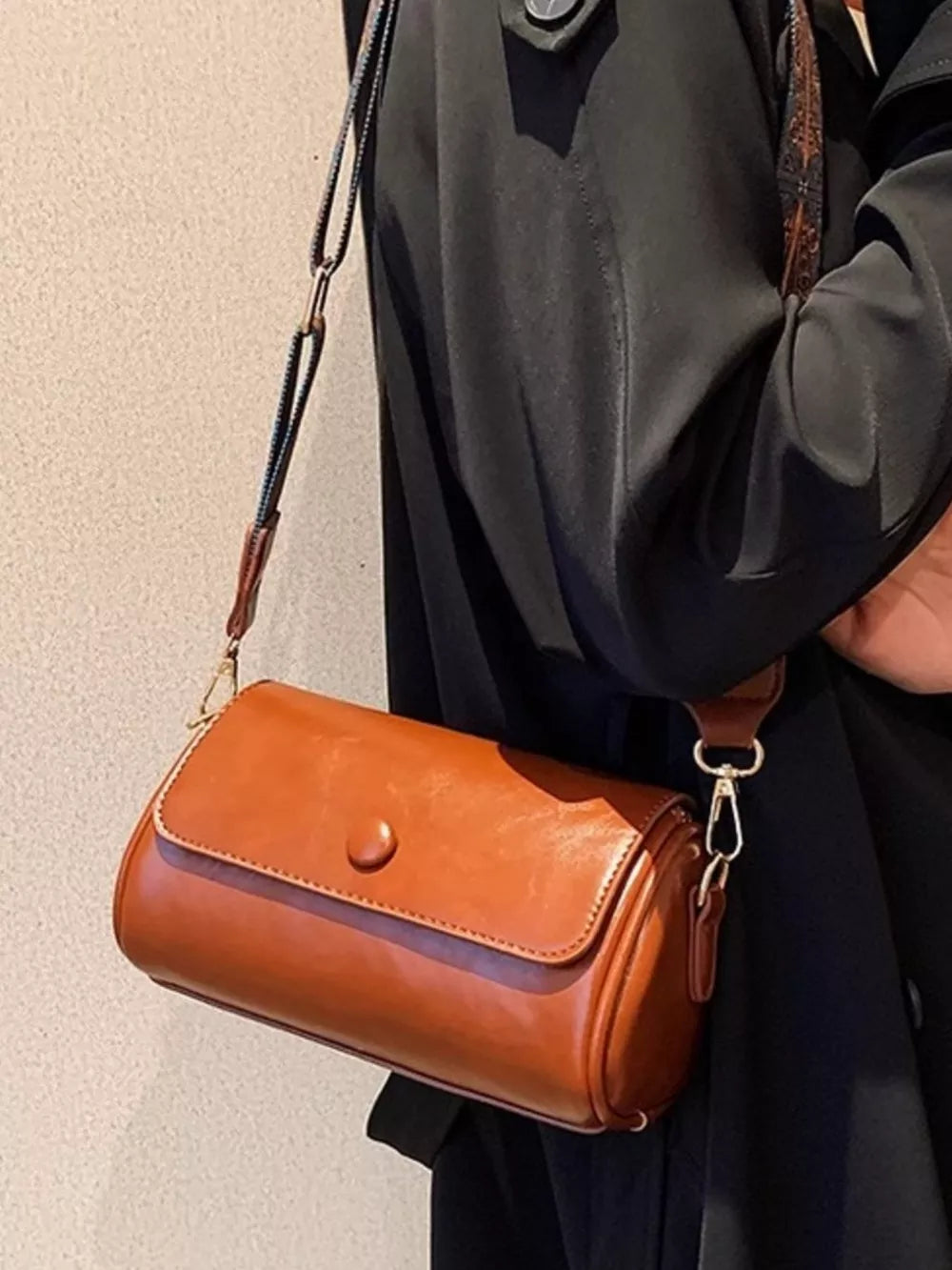 Brown leather mini crossbody bag with ethnic strap and button closure.