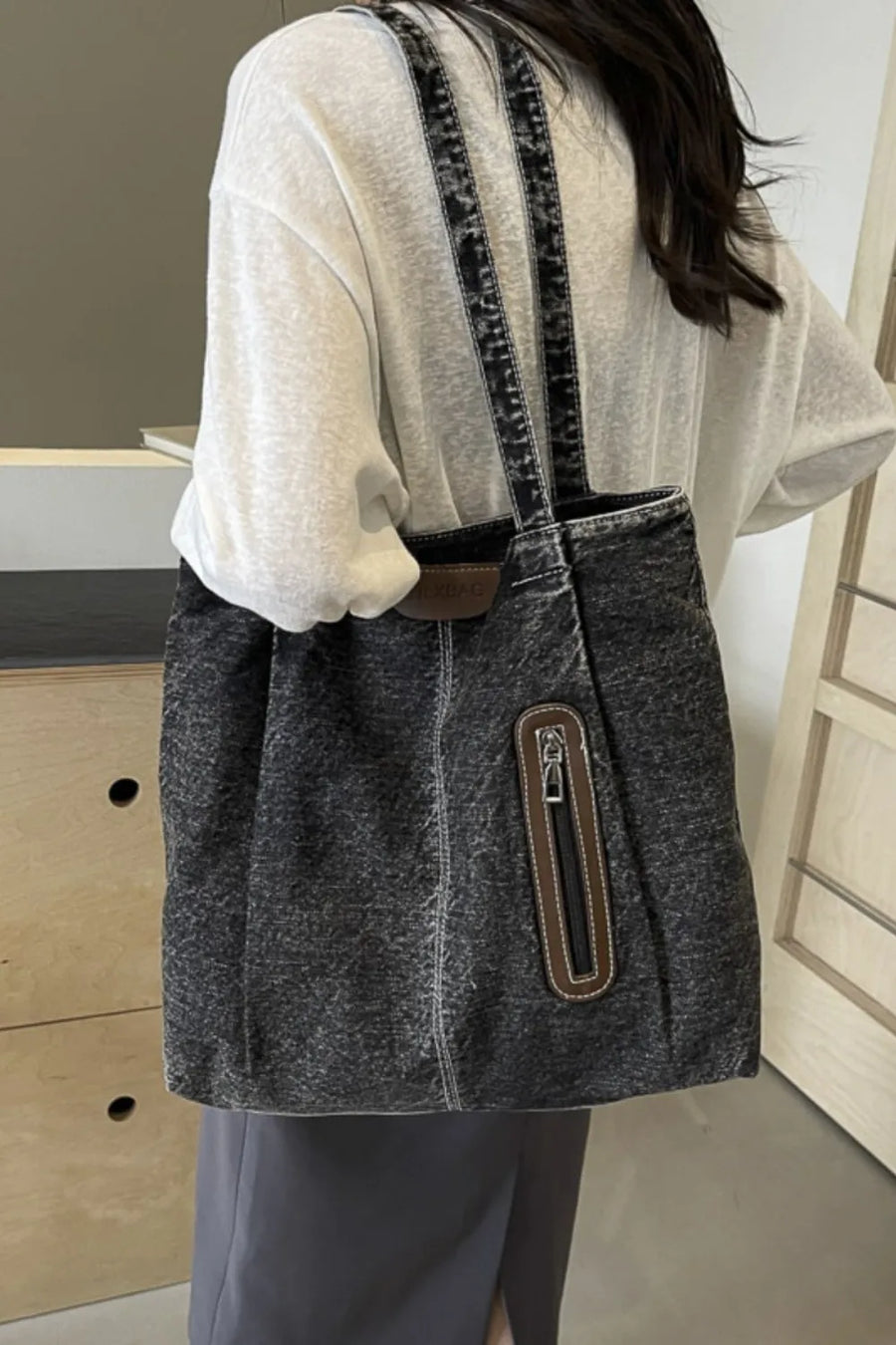 Denim tote bag in dark wash with leather trim and front zipper pocket.