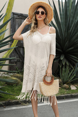 Cream crochet cover-up with fringe hem and V-neck, styled with a straw hat and bag.