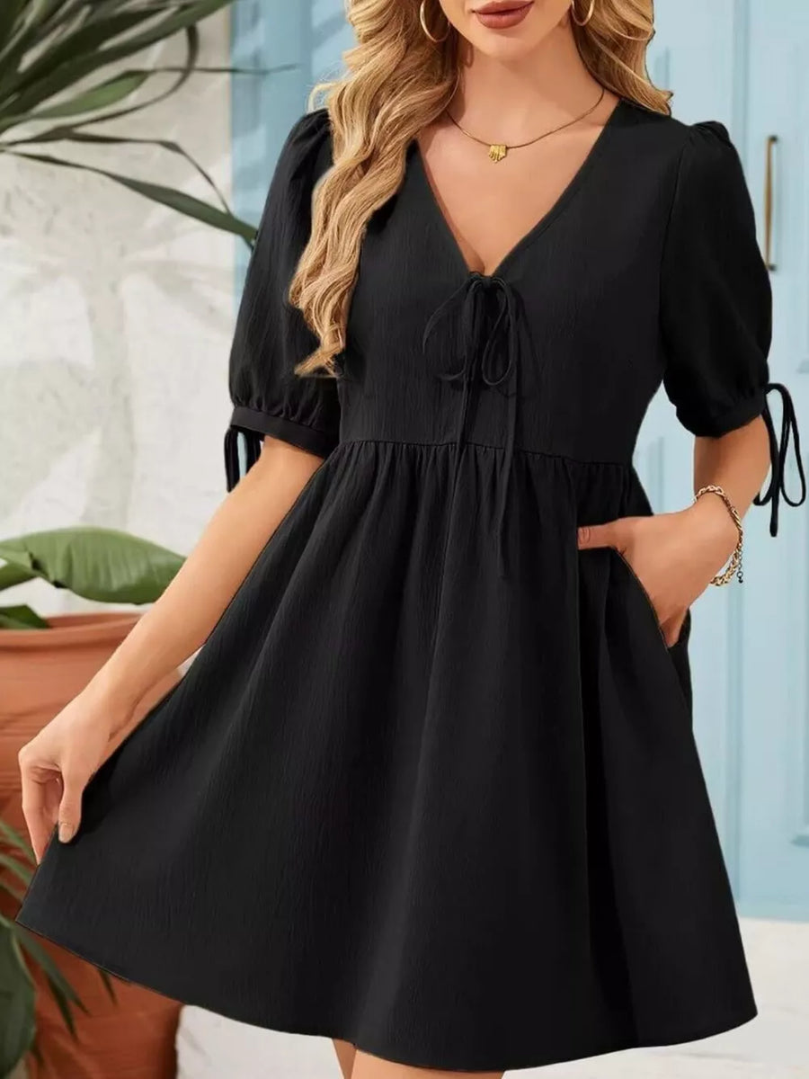 Black mini dress with tie neck, puff sleeves, and pockets.