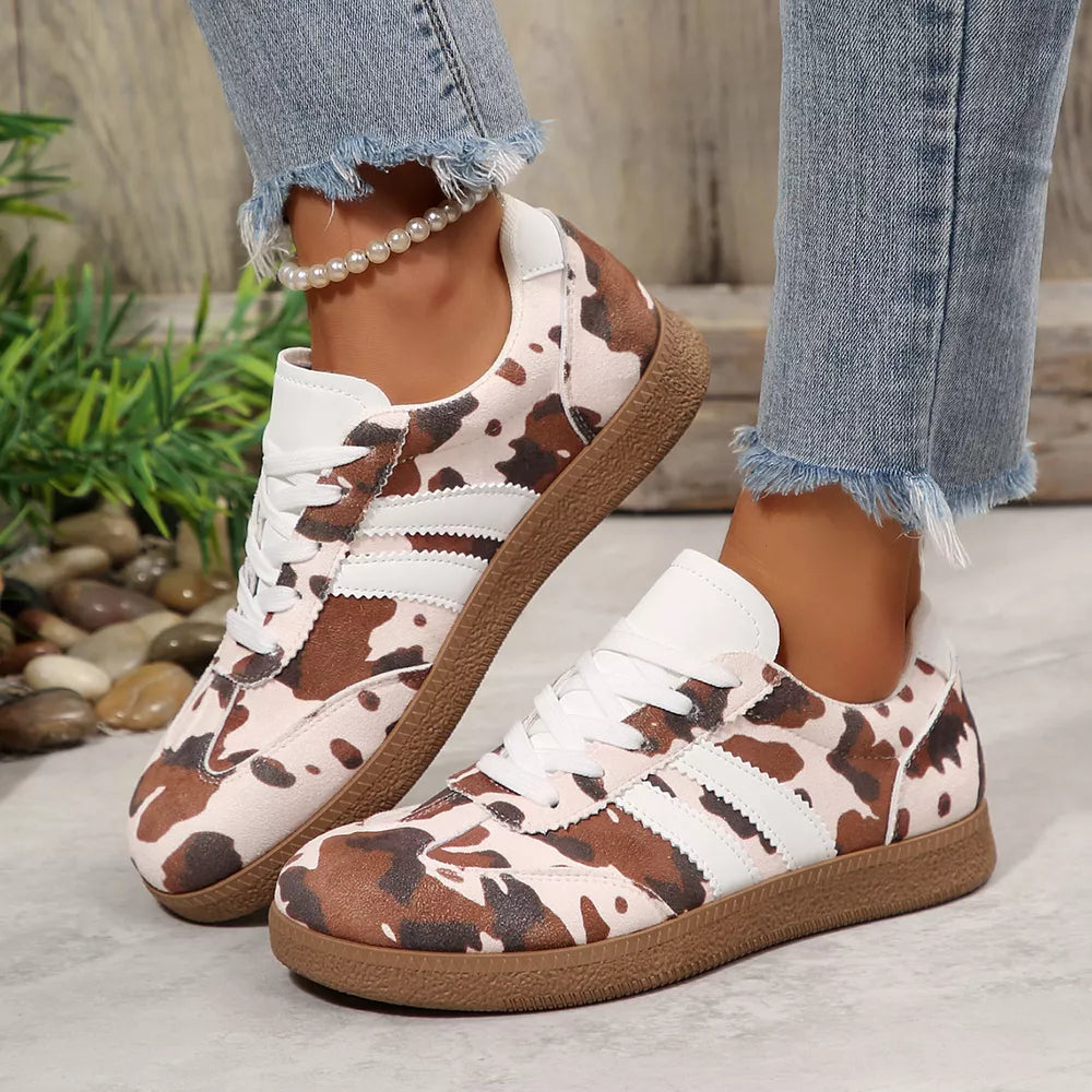 Trendy cow print low-top sneakers with white stripes and laces, brown sole.