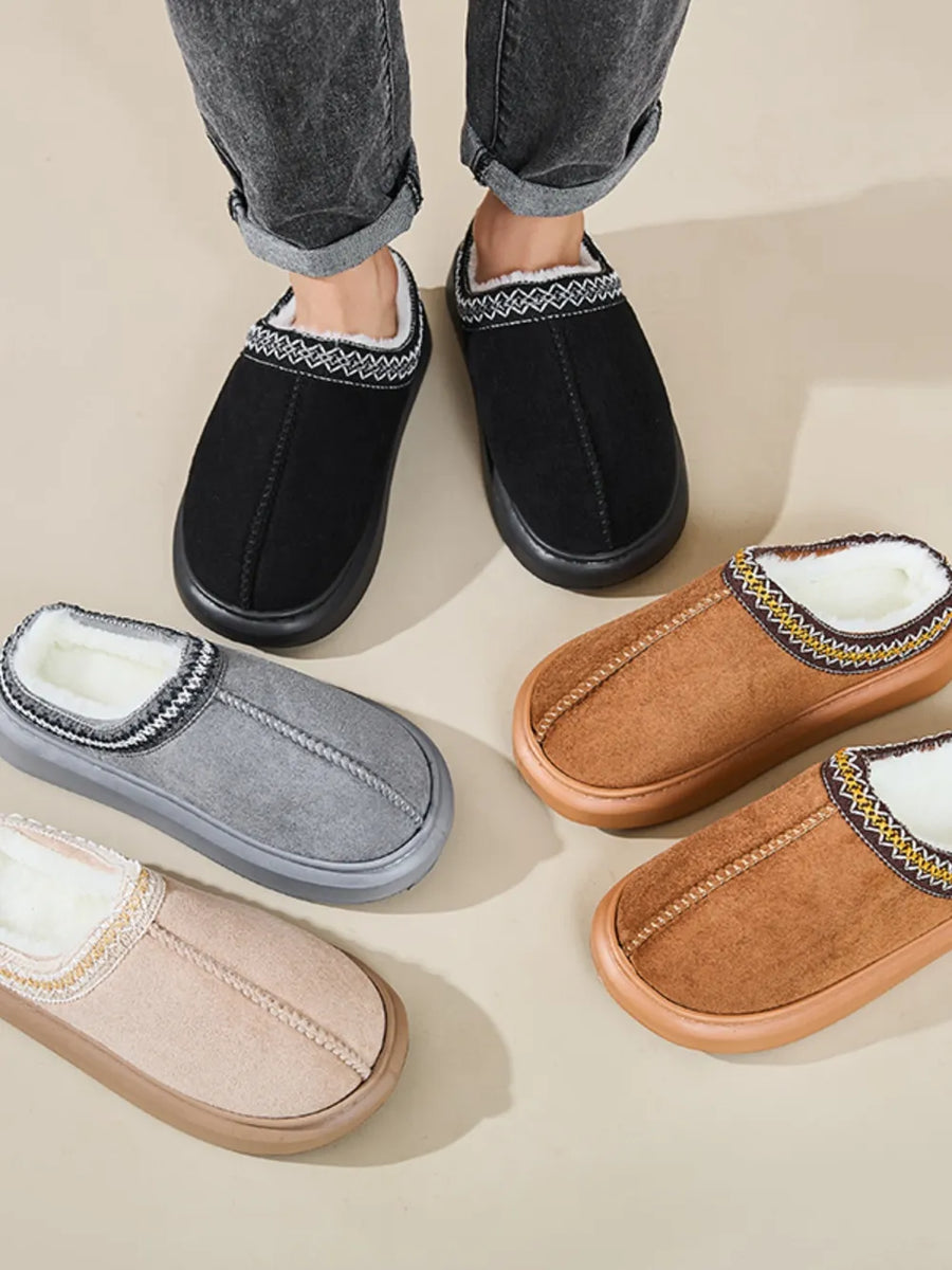 Embroidered trim shearling house slippers in black, gray, caramel, and tan with plush lining.