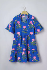 Blue tiered cotton dress with pink floral print, flutter sleeves, and tie neck.