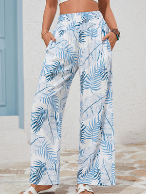 Tropical leaf print wide leg pants in white with blue foliage, featuring a smocked waistband and pockets.
