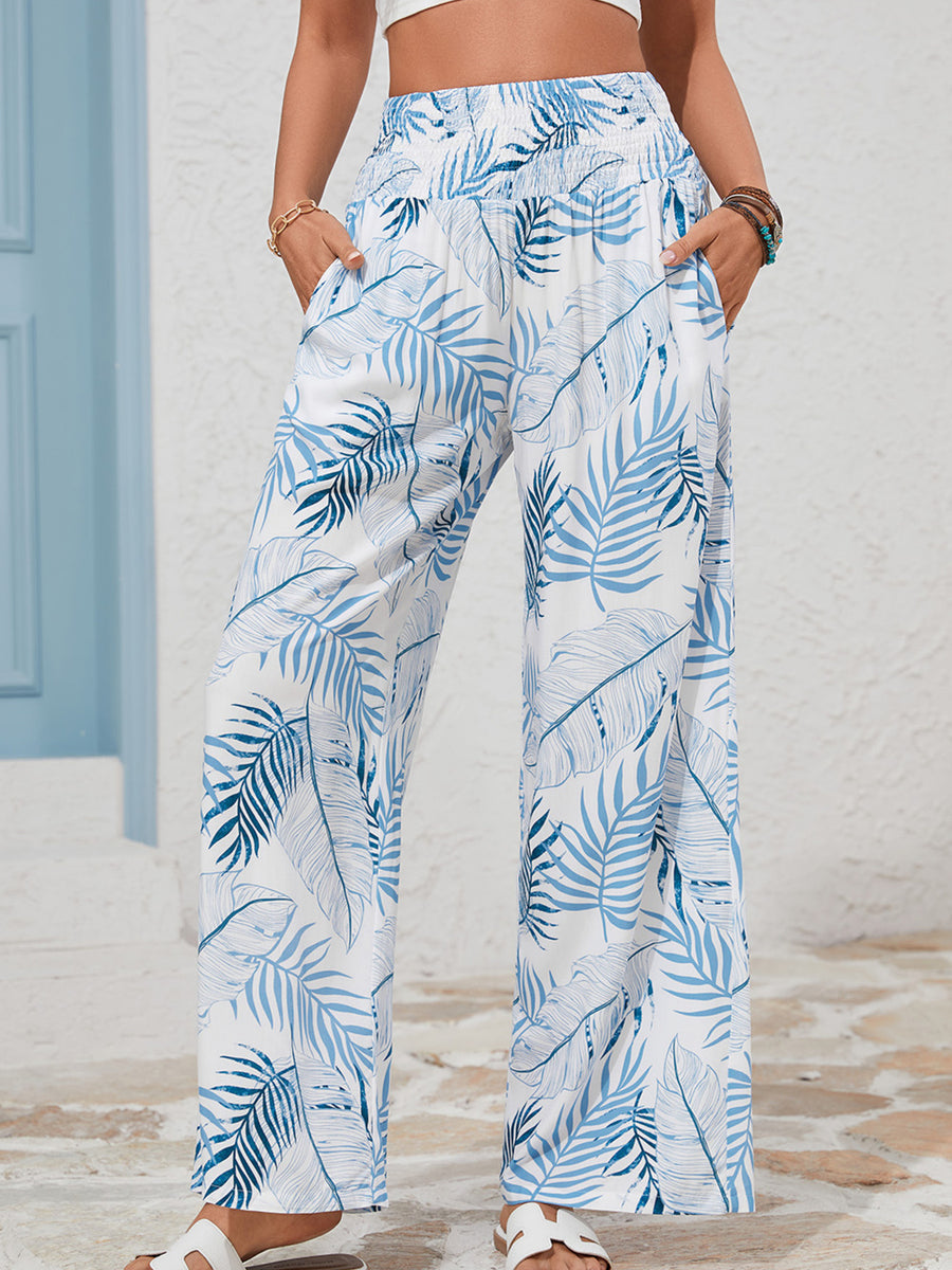 Tropical leaf print wide leg pants in white with blue foliage, featuring a smocked waistband and pockets.