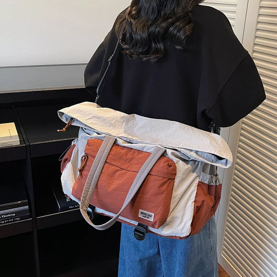Duffel bag in rust orange, cream, and grey colorblock with grey straps and buckle closure.
