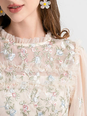 Embroidered floral tulle maxi gown with ruffled neckline and sleeves in a light peach hue.