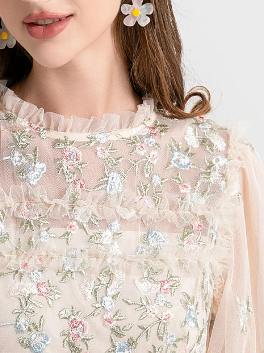 Embroidered floral tulle maxi gown with ruffled neckline and sleeves in a light peach hue.