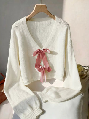 Beige acrylic knit V-neck cardigan with pink bow embellishment.