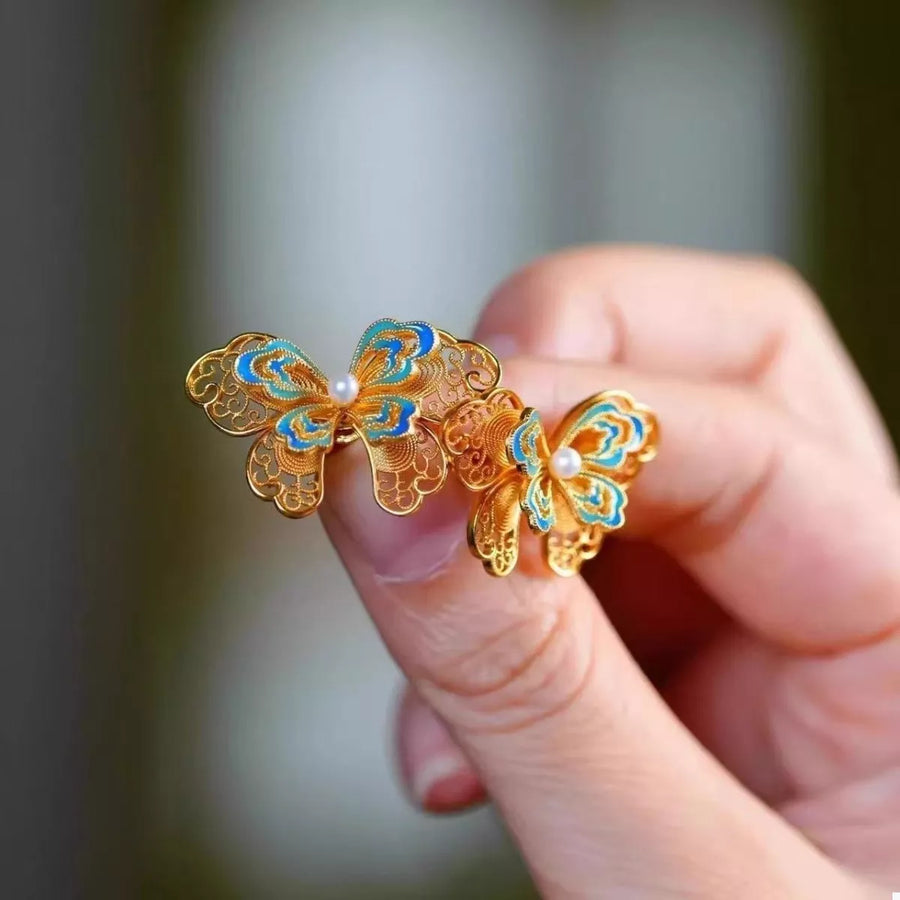 Elegant gold butterfly stud earrings with blue enamel detail and pearl accent.