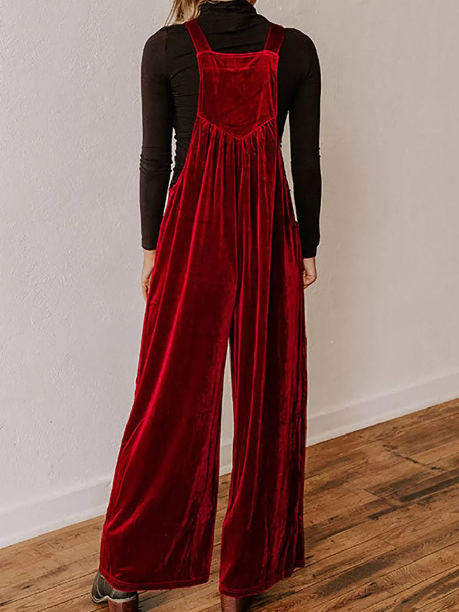 Burgundy velvet wide-leg romper with adjustable straps and a pleated bodice, worn over a black turtleneck.