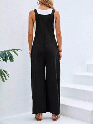 Black wide-leg romper with pockets and adjustable straps, worn with a white tank top.