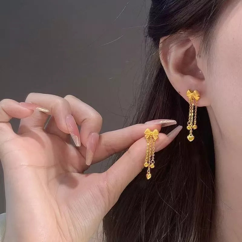 Gold bowknot tassel earrings with heart charms and chain detail.