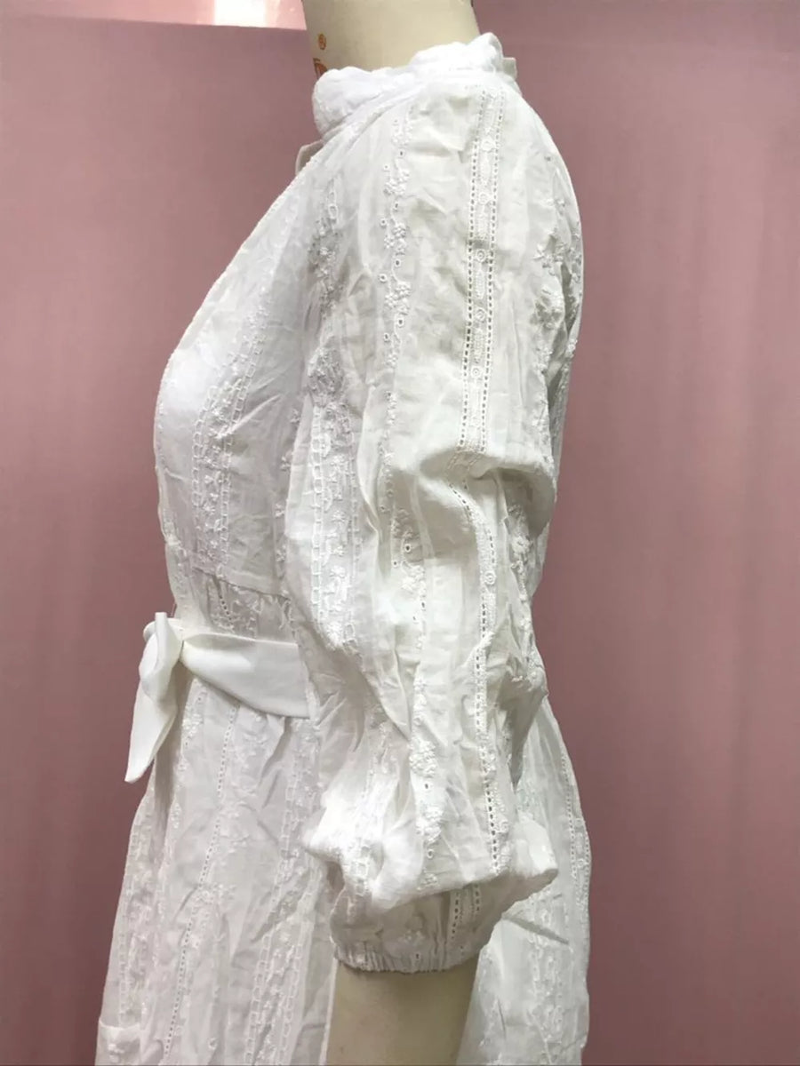 White eyelet dress with puff sleeves, high neck, and sash belt.