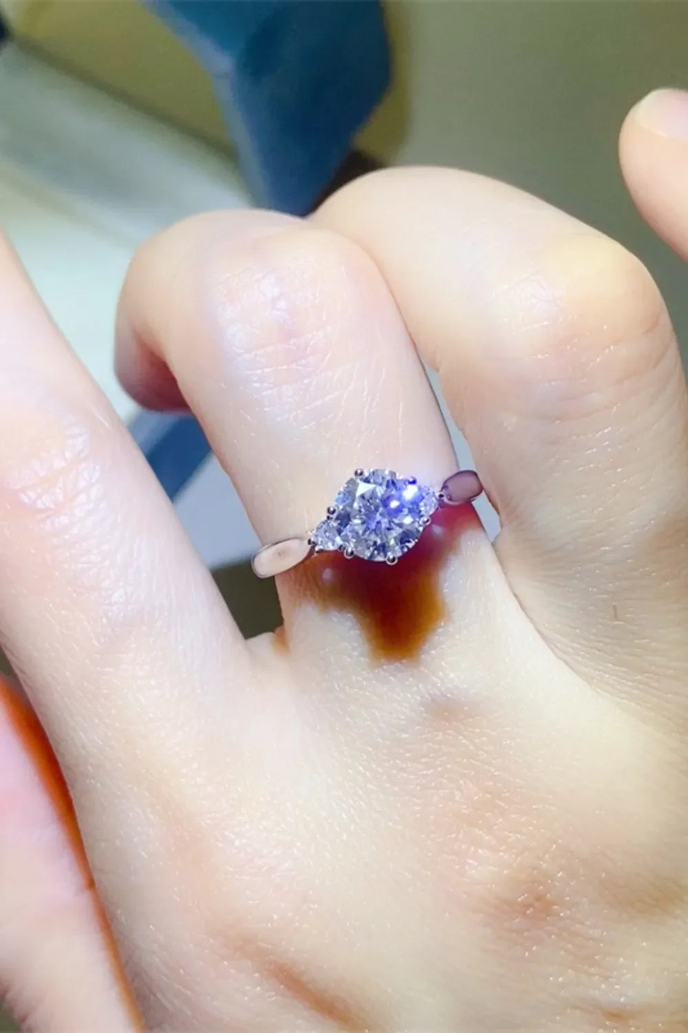 Silver moissanite trilogy engagement ring with a central round cut stone and two pear cut side stones.