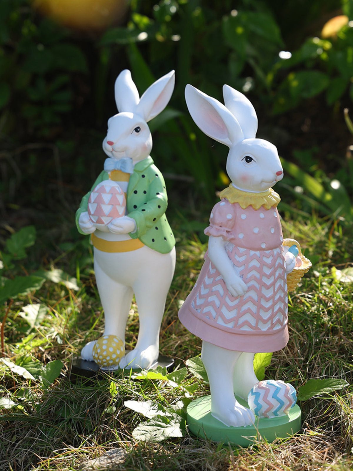 Easter bunny figurines in blush pink and gum leaf green, holding decorative eggs.