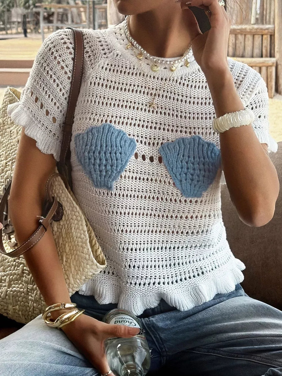 White crochet knit top with blue seashell appliqués and ruffled hem.