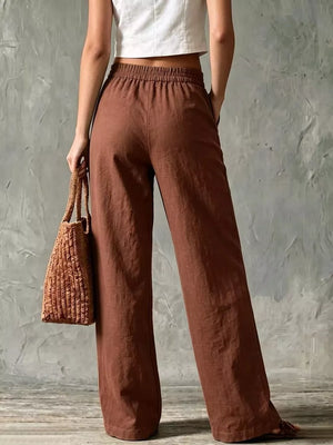Brown linen wide-leg pants with elastic waist and pockets, styled with a straw bag.