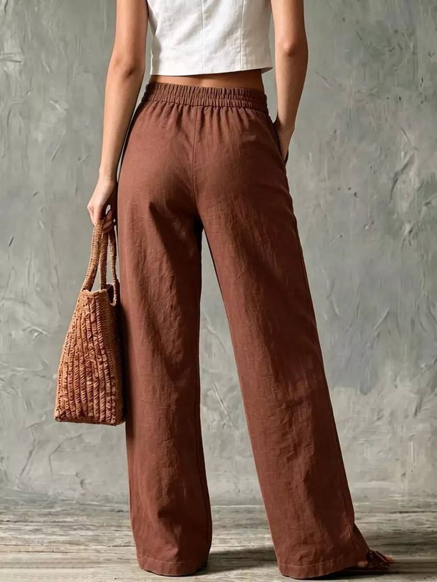 Brown linen wide-leg pants with elastic waist and pockets, styled with a straw bag.