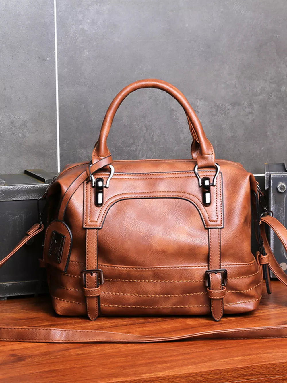 Brown leather half-moon handbag with buckle details and top handles.
