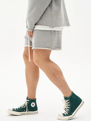 Gray fleece lounge shorts with raw edge hem and drawstring, paired with a matching sweatshirt.